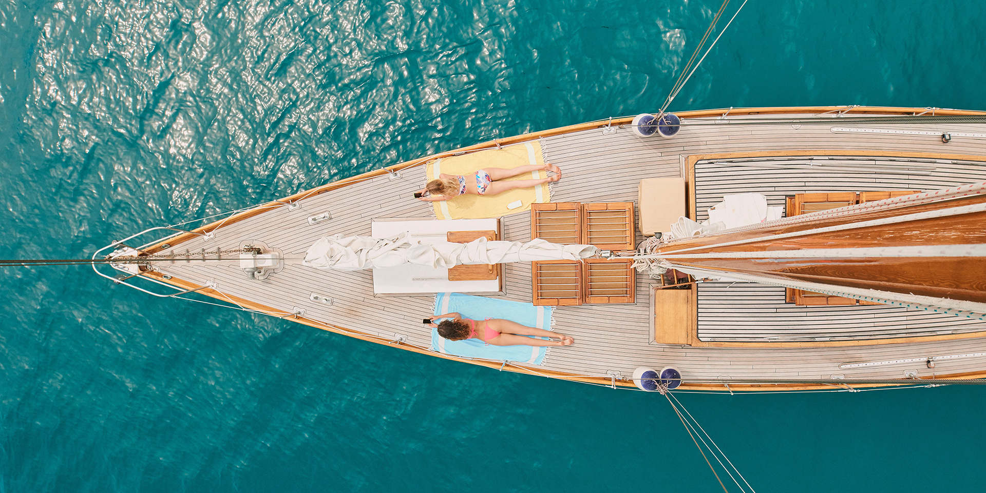 Two women in bikinis lying on yacht sunbathing using cellphones from above. Friends on holiday sunb.